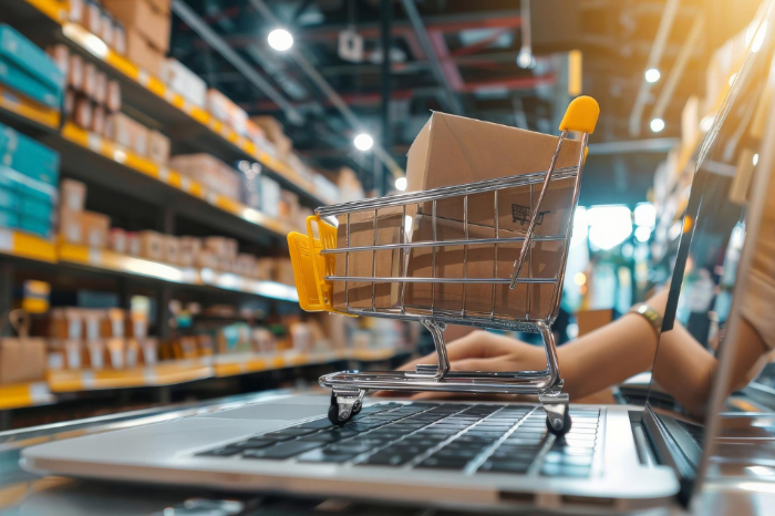 Carrito de compras pequeño con cajas de cartón colocado sobre el teclado de una computadora portátil en un almacén.