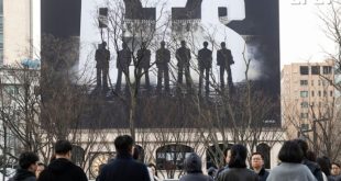 Una marea de fans del ARMY de BTS con lightsticks morados llenando la plaza Gwanghwamun en Seúl frente al escenario del concierto de retorno.