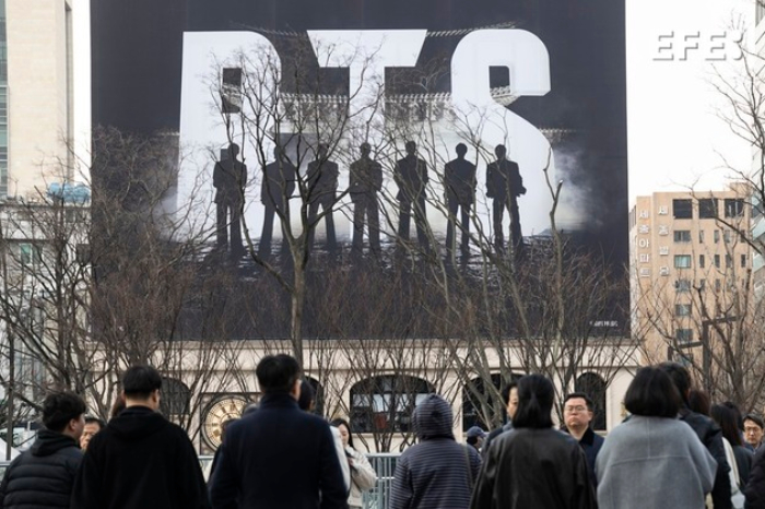 Una marea de fans del ARMY de BTS con lightsticks morados llenando la plaza Gwanghwamun en Seúl frente al escenario del concierto de retorno.