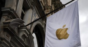 Bandera blanca con el logotipo de Apple colgada en la fachada de un edificio institucional bajo un cielo nublado.