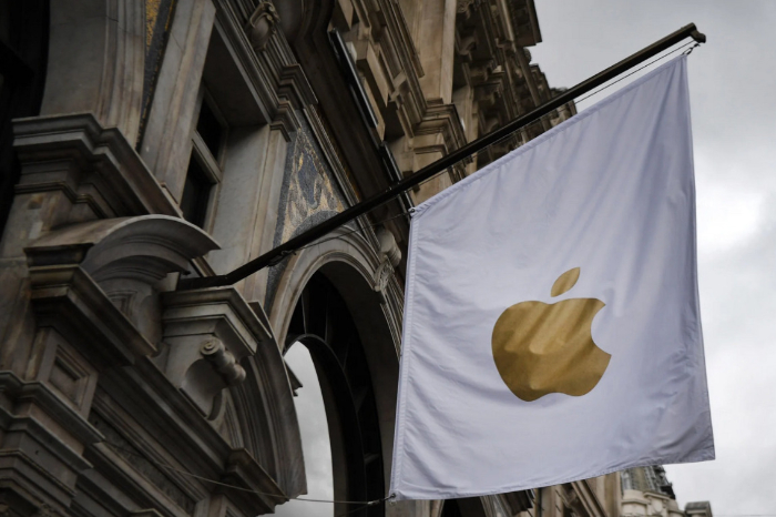Bandera blanca con el logotipo de Apple colgada en la fachada de un edificio institucional bajo un cielo nublado.
