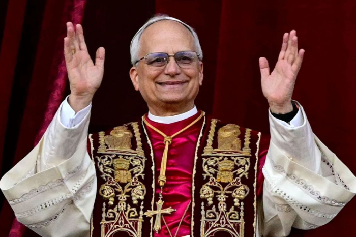 El papa León XIV con vestiduras litúrgicas rojas y blancas saludando con ambas manos desde un balcón.