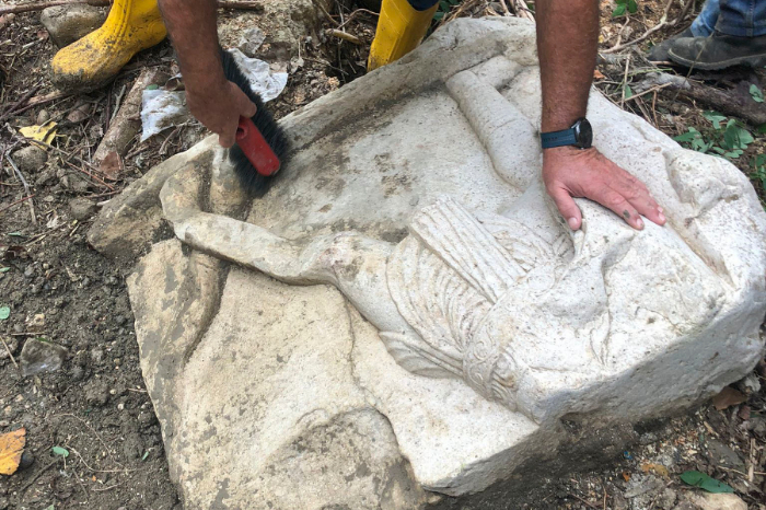 Arqueólogo limpiando con un cepillo un bloque de piedra caliza con relieves de la época romana hallado en Apollosa, Italia.