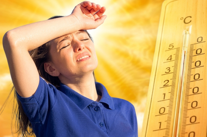 Mujer joven sufriendo por el intenso calor junto a un termómetro que marca temperaturas altas bajo el sol.