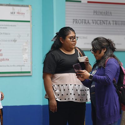 Madres y padres de familia conversando afuera de una escuela secundaria en la Ciudad de México.