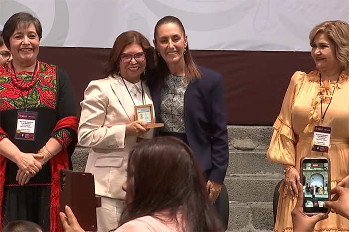 La presidenta Claudia Sheinbaum entrega un reconocimiento a una maestra durante el evento del Día del Maestro en Ciudad de México.
