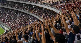 Afición mexicana de pie en las tribunas de un estadio alzando los brazos durante un partido oficial.
