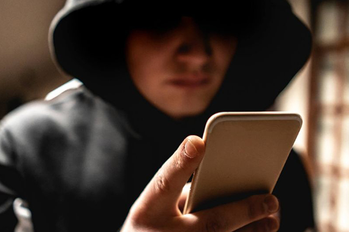 Hombre con el rostro cubierto usando un teléfono.