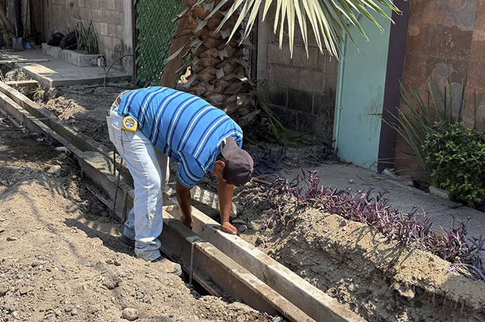 Trabajadores de la construcción aplican concreto hidráulico durante la pavimentación de una calle urbana.