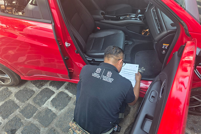 Personal operativo del Repuve colocando un holograma de seguridad en el parabrisas de un automóvil.