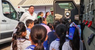 Estudiantes de primaria observando vehículos de emergencia, patrullas y camiones de bomberos en una exhibición educativa.