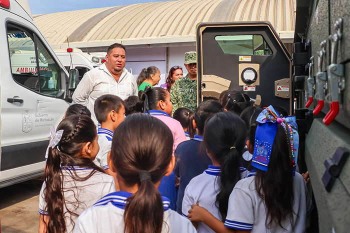 Estudiantes de primaria observando vehículos de emergencia, patrullas y camiones de bomberos en una exhibición educativa.