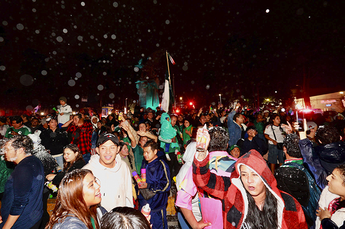 Multitud de aficionados celebrando la victoria de México bajo la lluvia en el Ángel de la Independencia.