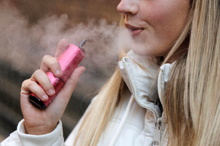 Persona joven utilizando un cigarrillo electrónico de sabores que afecta la expresión génica.