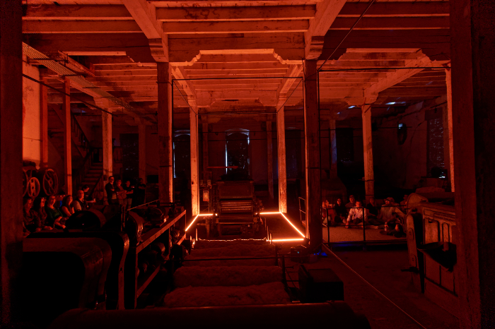 Instalación artística inmersiva interactiva en un antiguo complejo textil industrial de Michoacán con espectadores sentados al fondo.
