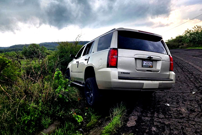 Vista trasera de una camioneta Chevrolet Tahoe color arena que se salió del camino en una zona de terracería y maleza en Puruándiro.