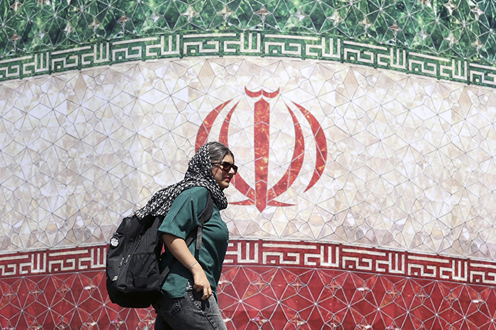 Una mujer iraní pasa junto a una valla publicitaria con la bandera nacional de Irán en la plaza Enqelab de Teherán, Irán.