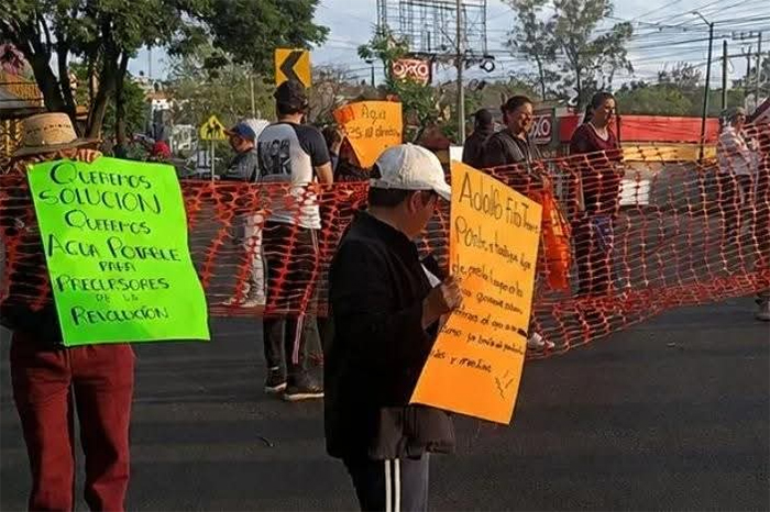 Manifestantes bloqueando el paso vehicular con pancartas sobre los carriles de un libramiento urbano.