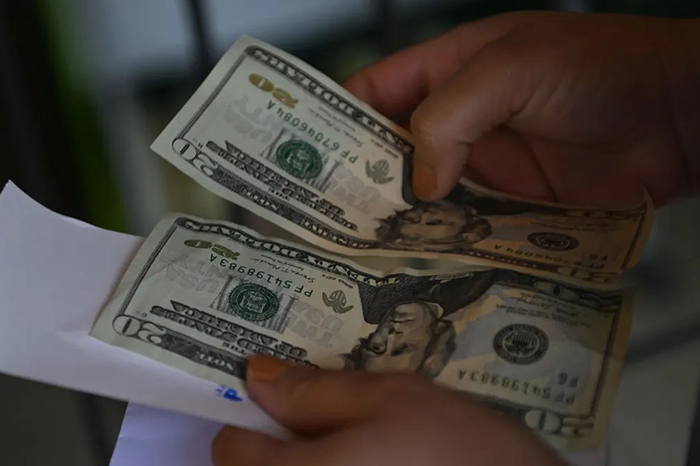 Manos de un ciudadano contando billetes de dólares estadounidenses sobre una mesa en una ventanilla de cobro.