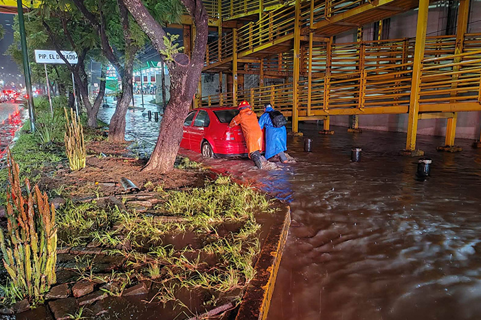 Personal de Protección Civil de Michoacán y Bomberos de Morelia auxiliando a conductores en una avenida inundada tras la tormenta.