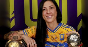 Futbolista profesional sonriendo en una cancha de fútbol con la camiseta de su equipo.