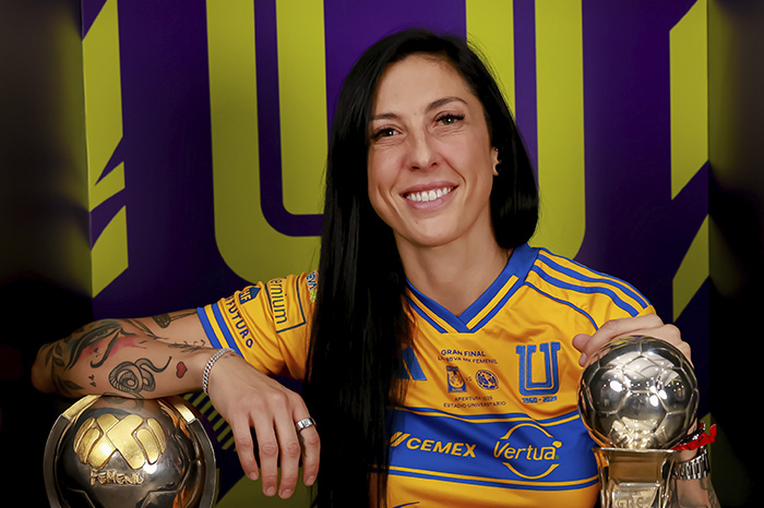 Futbolista profesional sonriendo en una cancha de fútbol con la camiseta de su equipo.