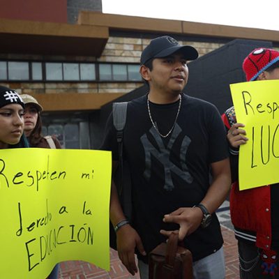Jóvenes con pancartas exigiendo respeto a sus derechos educativos frente a un recinto universitario.