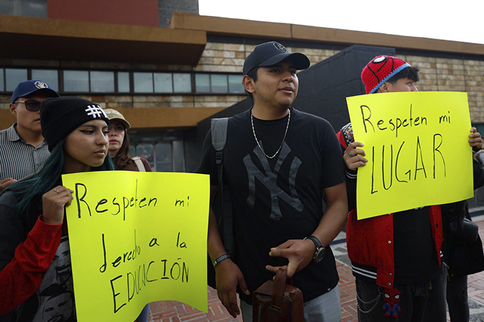 Jóvenes con pancartas exigiendo respeto a sus derechos educativos frente a un recinto universitario.