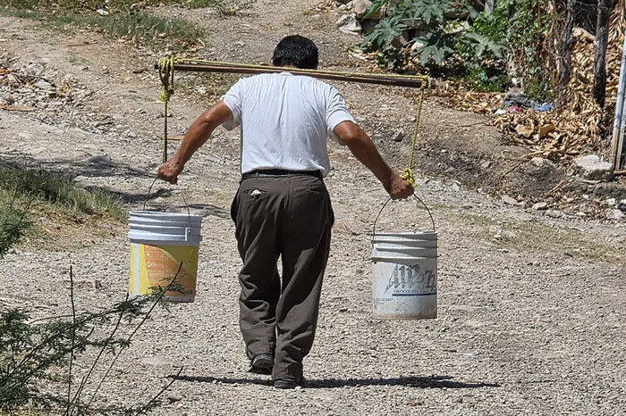 Persona cargando baldes de agua para abastecerse ante la sequía.