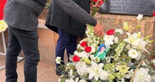 Manos colocando flores y un arreglo floral conmemorativo junto a la placa en honor a las víctimas del atentado del 15S en Morelia.