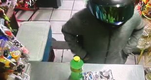 Captura de cámara de seguridad mostrando a un motociclista con casco amagando en una tienda de abarrotes.