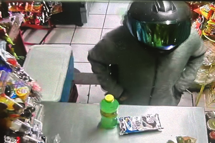 Captura de cámara de seguridad mostrando a un motociclista con casco amagando en una tienda de abarrotes.