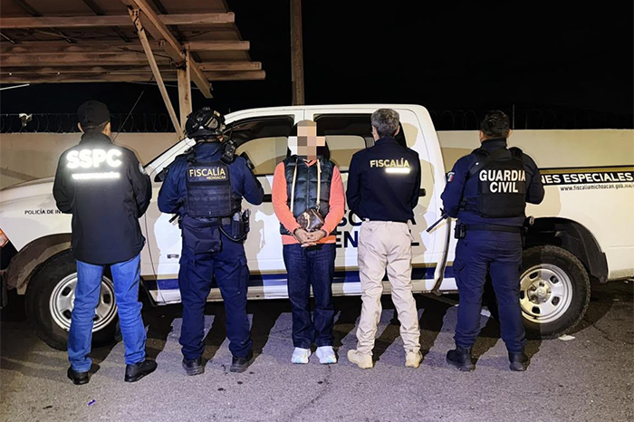 Elementos de la Policía de Investigación y agentes migratorios custodia a un detenido en una terminal aérea.